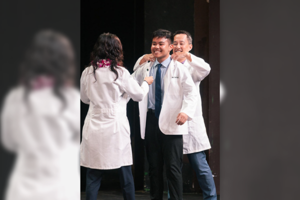 MD 2027 candidate, Tyrone John Sumibcay (center) receiving his white coat from his Learning Community mentors, Drs. Jimmy Chen (behind) and Jannet Lee-Jayaram (front.)